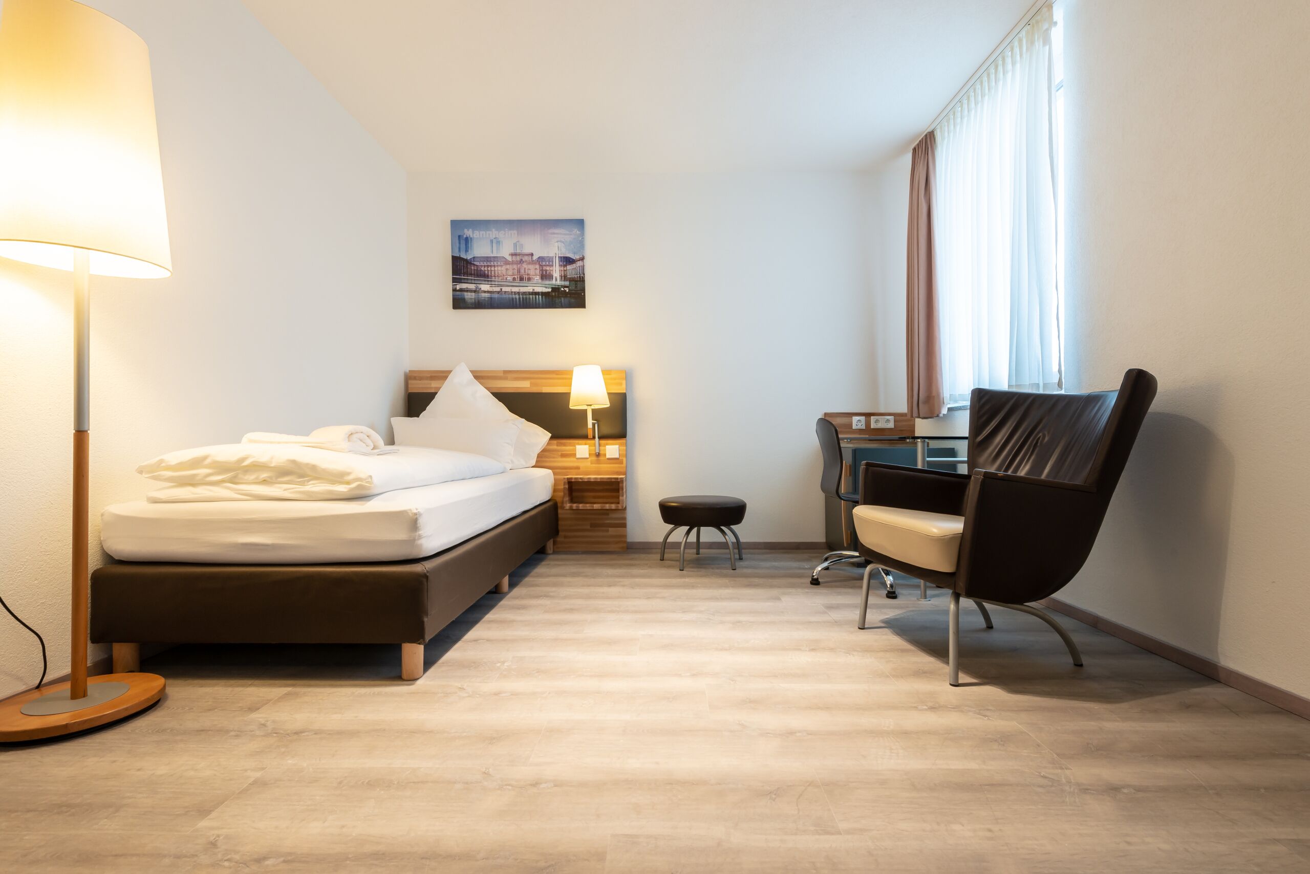 A hotel room with a bed, desk, chair, and a lamp.