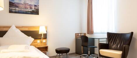 A hotel room with a bed, a desk, a chair, and a view of a cityscape.