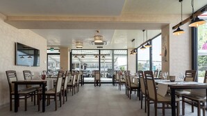 Un restaurante amplio con numerosas mesas y sillas, ventanas grandes y lámparas colgantes.