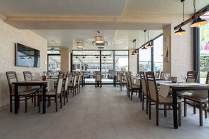 A spacious restaurant with multiple tables and chairs, large windows, and hanging pendant lights. - Hotel in Laisen (Reutlingen)