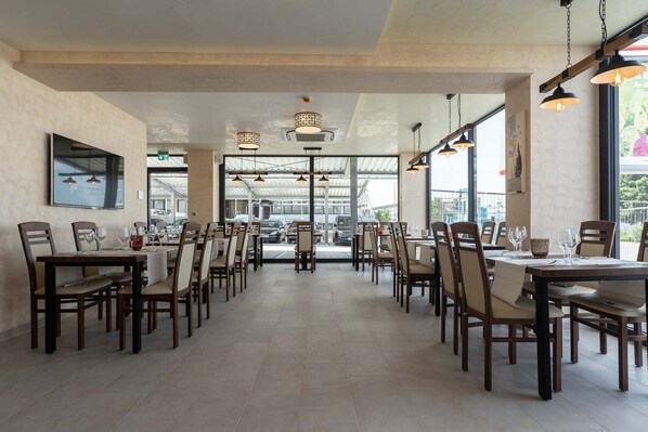 A spacious restaurant with multiple tables and chairs, large windows, and hanging pendant lights. - Hotel in Laisen (Reutlingen)