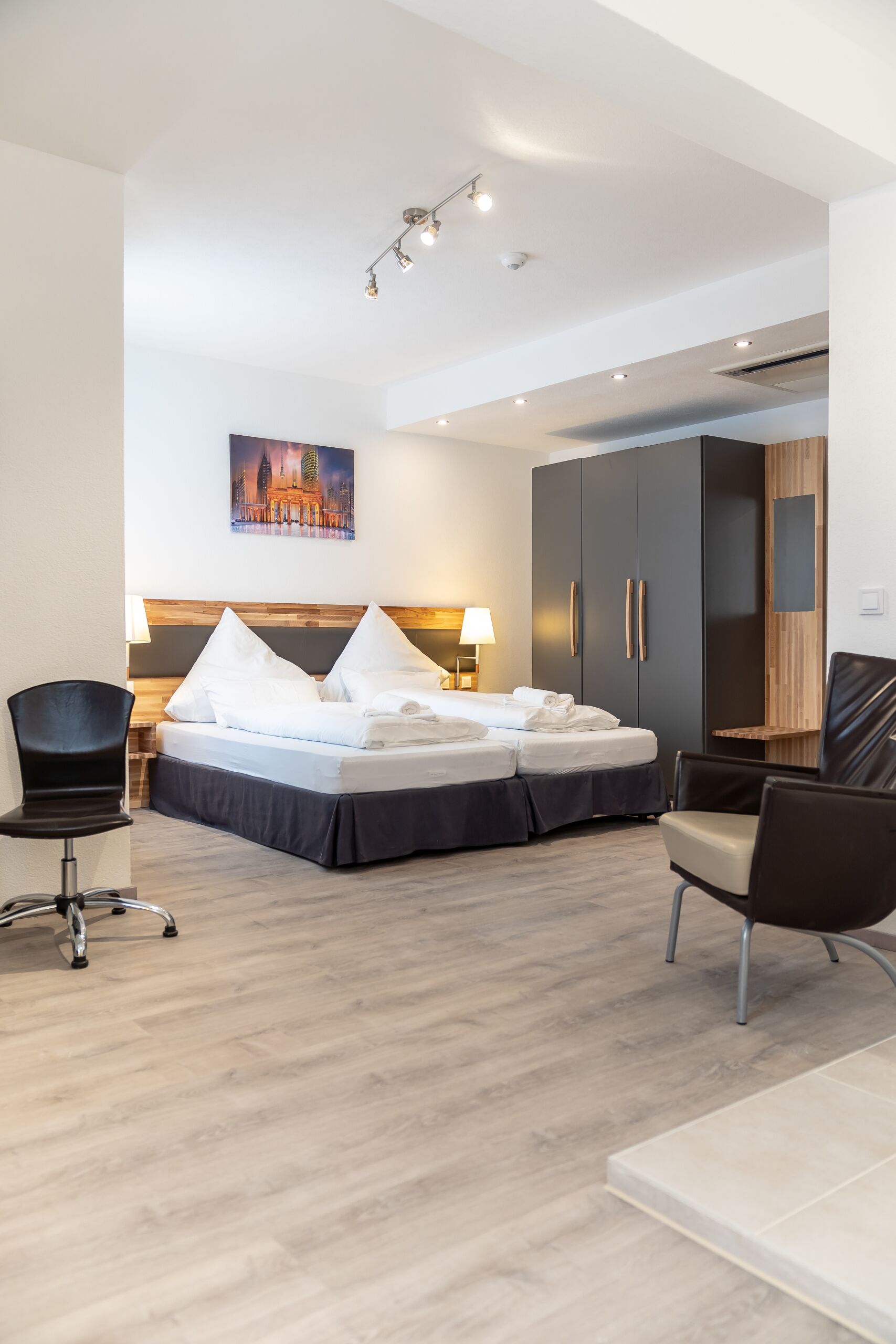 A modern hotel room with a bed, two chairs, a desk, and a wardrobe.