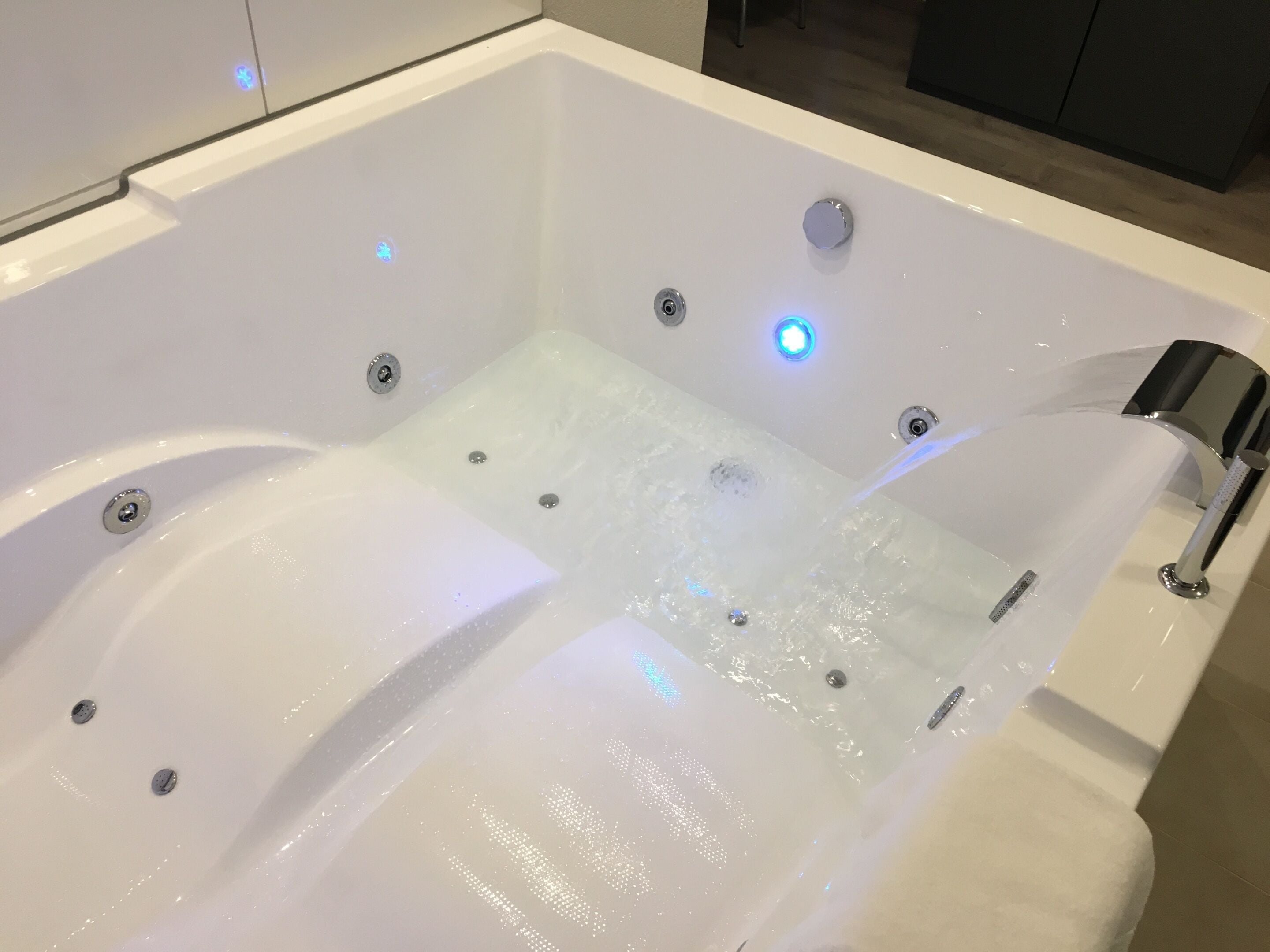A modern bathtub with multiple jets, a built-in seat, and a handheld showerhead.