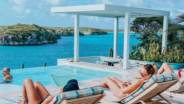 A poolside area with lounge chairs and a covered seating area overlooking a body of water.