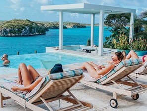 Zona junto a la piscina con sillones de descanso y un área de estar cubierta con vistas a un cuerpo de agua.