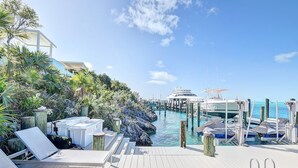 A wooden deck with lounge chairs, a marina with boats, and a clear blue sky.