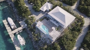 An aerial view of a coastal property with a large house, a swimming pool, and a dock with boats.