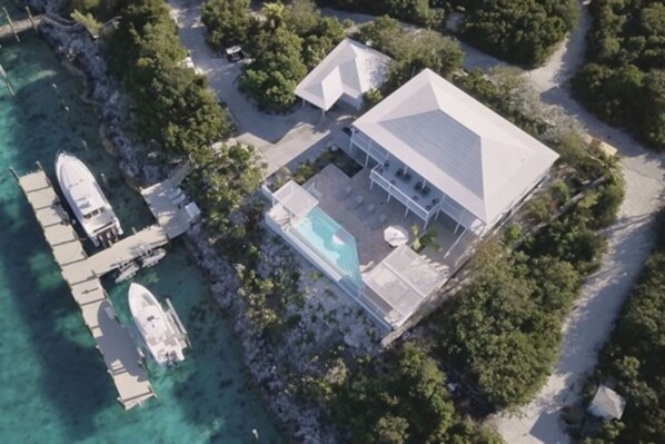 Vista aérea de una propiedad costera que incluye una casa grande, una piscina y un muelle con barcos.