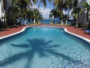 Ein klarer Pool mit einer gefliesten Kante, umgeben von Palmen und Blick auf den Ozean.