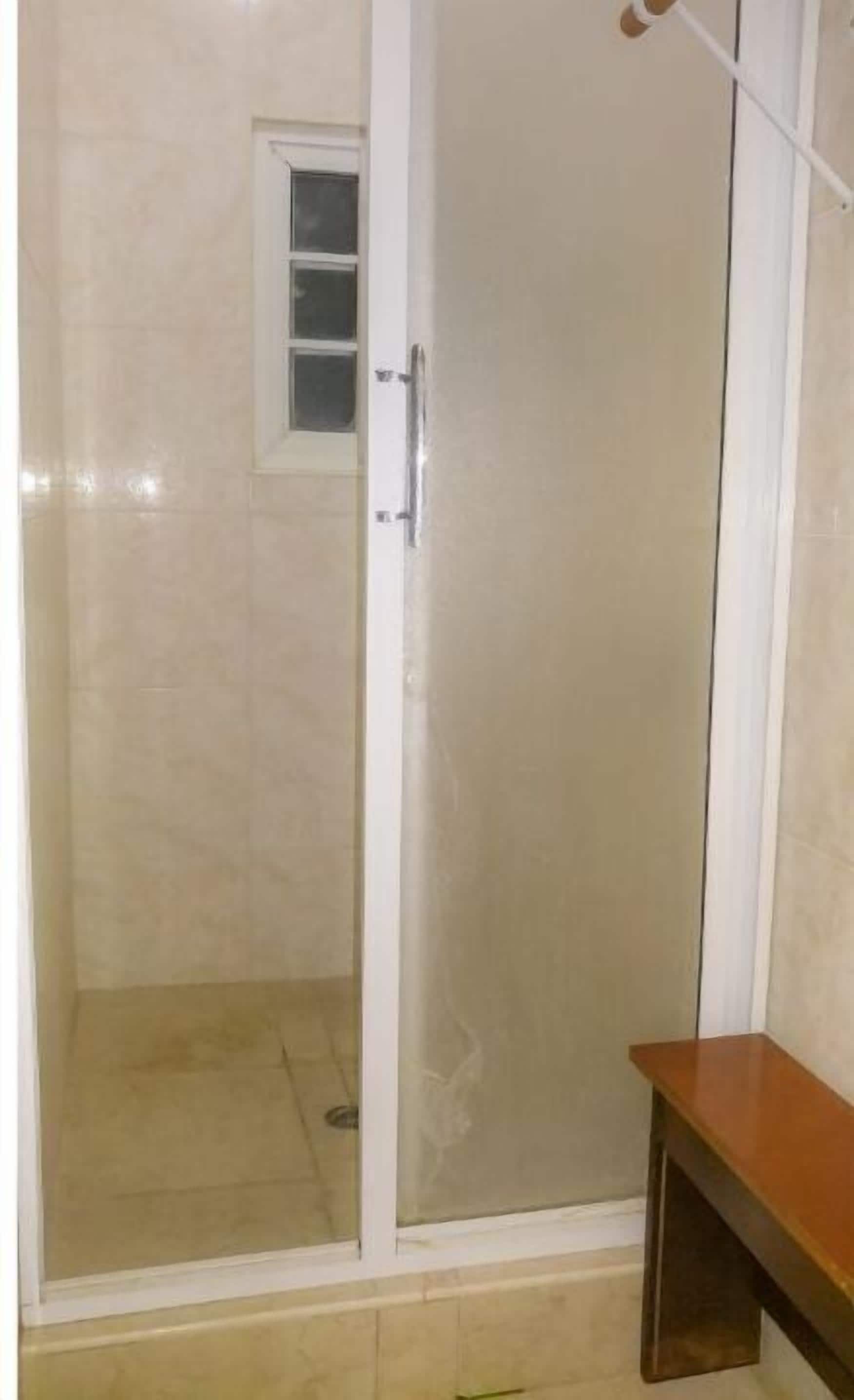 Een badkamer met een glazen douchecabine, een klein raam en een houten bankje.