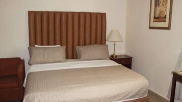 A neatly made bed with a headboard, a bedside lamp, and a framed picture on the wall.