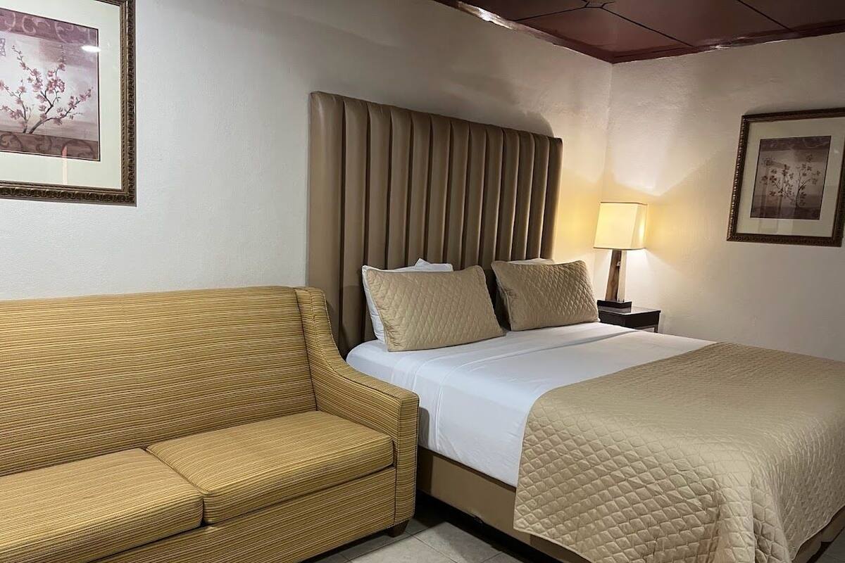 A hotel room with a bed, a sofa, a nightstand, and a lamp.