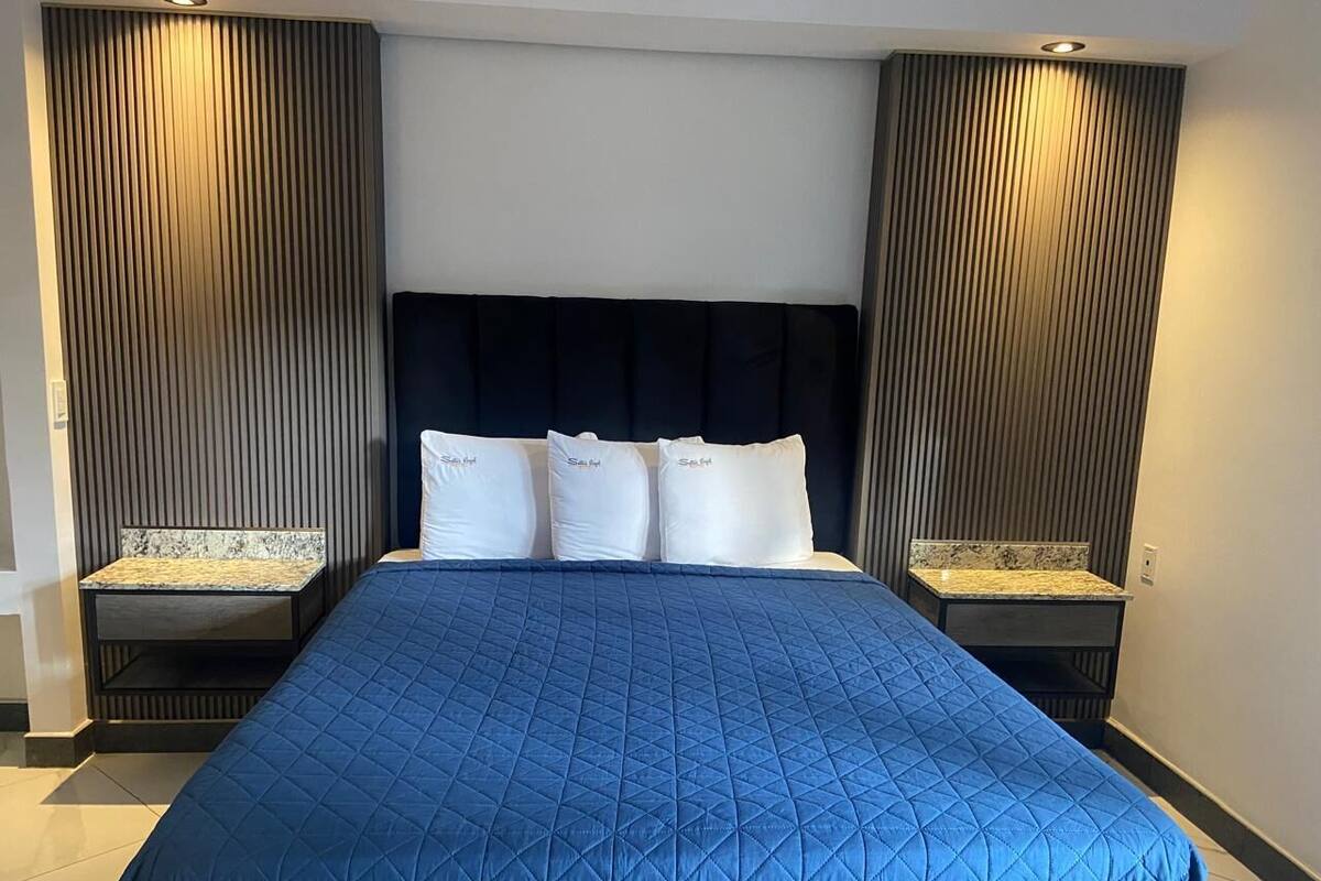 A hotel room with a large bed, dark headboard, and two nightstands with marble tops.