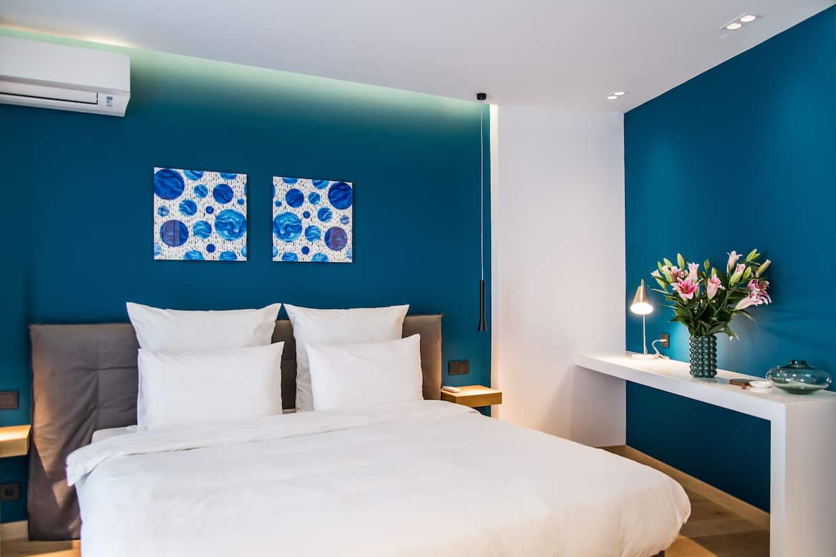 Ein modernes Schlafzimmer mit einem großen Bett, zwei an der Wand befestigten Gemälden, einem Nachttisch mit Blumenvase und einer Klimaanlage.