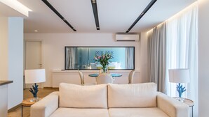 Et moderne hotelværelse med sofa, spisebord med stole, vase med blomster og et stort vindue med gardiner.