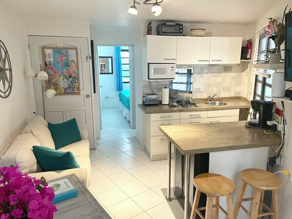 A compact living space with a kitchenette, a dining area, and a bedroom visible through an open door.