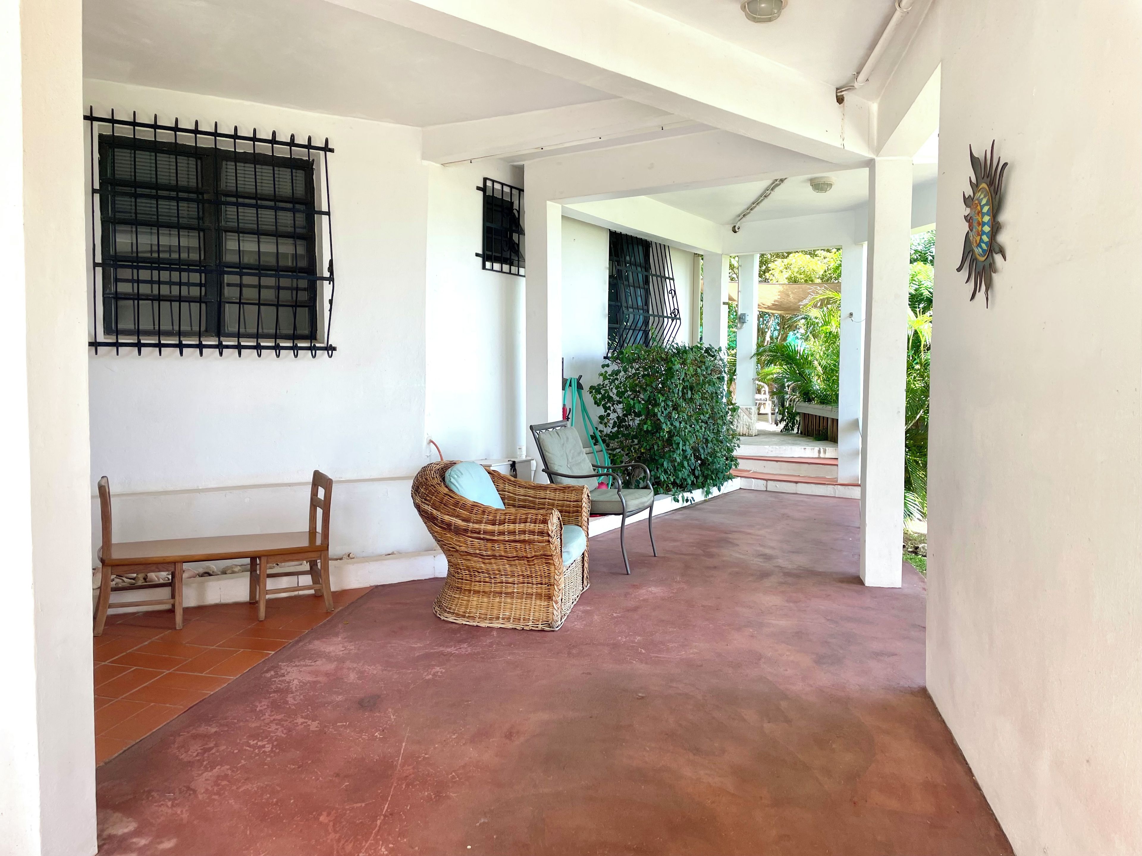 Espaço coberto ao ar livre com um banco, móveis de vime e um vaso de planta.