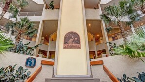 A multi-level atrium with a central column featuring a 'Sandcastles' sign, surrounded by palm trees and a blue plaque on the left. - Breathtaking View of the Atlantic Ocean & Beach (Fernandina Beach)
