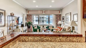 A spacious living area with a large wooden coffee table, green and beige sofas, and a view of the city through large windows. - Breathtaking View of the Atlantic Ocean & Beach (Fernandina Beach)