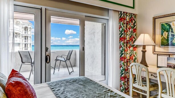 A hotel room with a bed, a desk, two chairs, a view of the beach, and a tropical-themed curtain. - Breathtaking View of the Atlantic Ocean & Beach (Fernandina Beach)