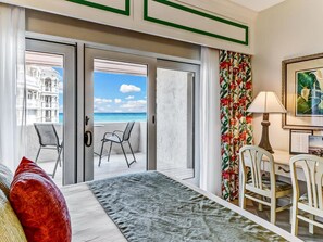A hotel room with a bed, a desk, two chairs, a view of the beach, and a tropical-themed curtain. - Breathtaking View of the Atlantic Ocean & Beach (Fernandina Beach)