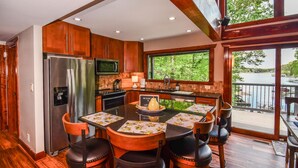 A modern kitchen with a stainless steel refrigerator, microwave, and stove, a dining area with a table and chairs, and a large window overlooking a lake.