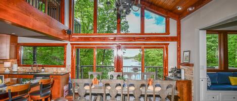 A spacious dining area with a high ceiling and large windows overlooking a lake.
