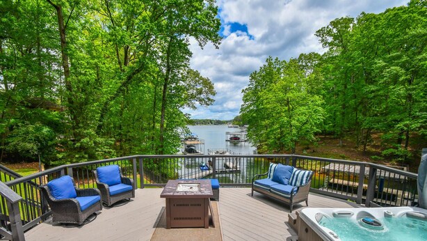 A deck with outdoor furniture, a hot tub, and a view of a lake with boats.