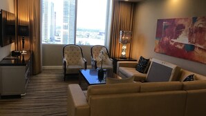 Une chambre d’hôtel avec une grande fenêtre, deux fauteuils, un canapé, une table basse, un téléviseur et un tableau au mur.