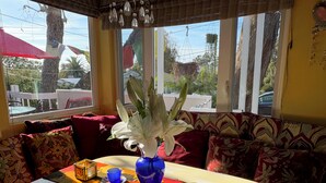 A cozy seating area with a table set for tea, a vase with white flowers, and a view of the outside through large windows. - Exquisite L.B. House Within Walking Distance to Beach and Town (Laguna Beach)