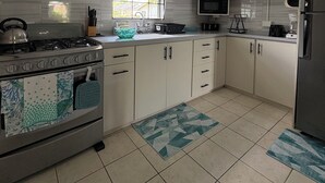 Une cuisine avec des meubles blancs, une cuisinière à gaz, un four à micro-ondes et un réfrigérateur.