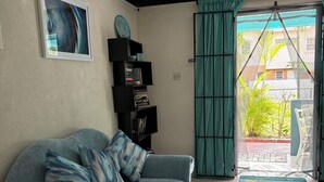 Un salon avec un canapé, une bibliothèque et une vue sur l’extérieur, visible à travers une porte.