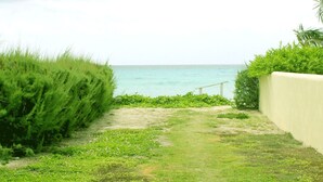 Un sentier menant à une plage, bordé d’une rambarde et d’une végétation luxuriante d’un côté.