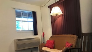 A room with a window, an air conditioner, a wicker chair with red cushions, and a hanging lamp. - Room 3-Historic Little Switzerland - (Jasper)