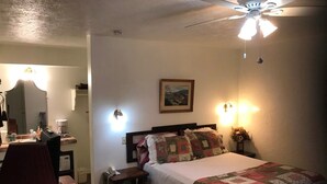 A bedroom with a bed, a desk with a chair, a ceiling fan, and a nightstand with a lamp. - Room 3-Historic Little Switzerland - (Jasper)