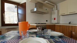 Une table à manger dressée avec des assiettes et des verres, une cuisinière à gaz et des meubles de rangement en bois dans une cuisine.