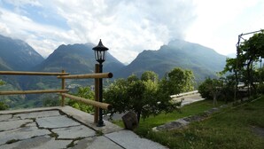 Un chemin de pierre mène à une balustrade en bois qui surplombe un paysage montagneux, avec une rue et de la végétation.