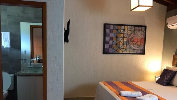 A bedroom with a bed, a painting on the wall, and a bathroom visible through an open door.