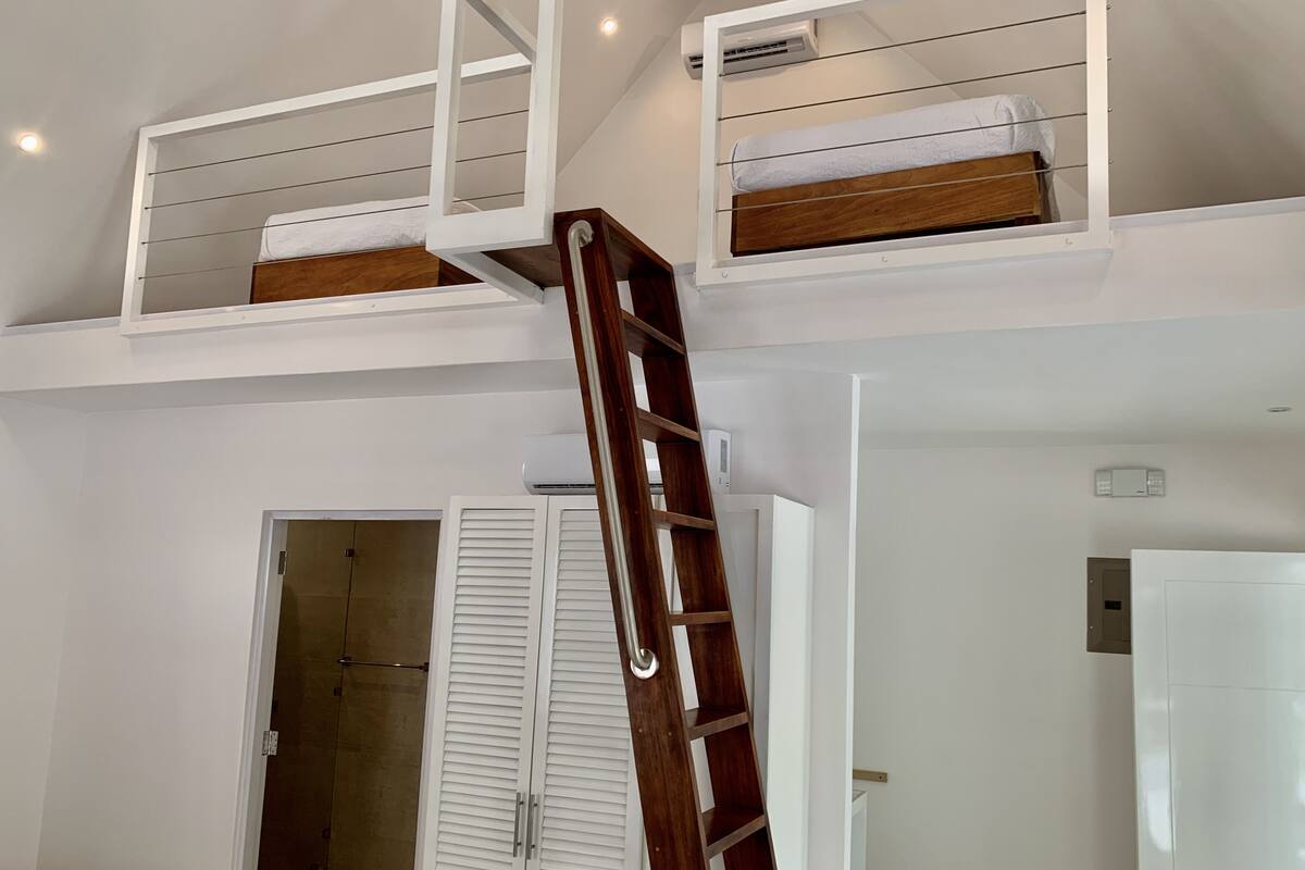 A room with a loft bed, a wooden ladder, and a white wardrobe.