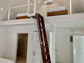 Una habitación con cama tipo litera, una escalera de madera y un armario blanco.