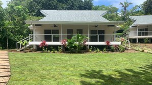 A two-story house with a covered porch, a small garden with tropical plants, and a wooden deck. - Aves Hotel & Resort - Retreat Center (Cóbano)