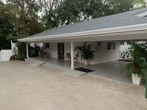 Un espacio exterior techado con piso de baldosas, una zona de estar cubierta con sillas y plantas en macetas.