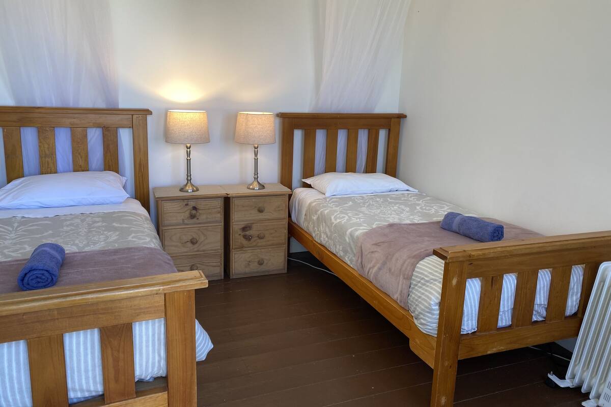 Una habitación doble con dos camas de madera, cada una con cabecera, mesitas de noche, lámparas y un pequeño aparador.