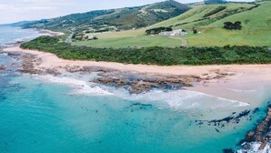 Paisagem costeira com uma praia, águas turquesa cristalinas e colinas suaves ao fundo.