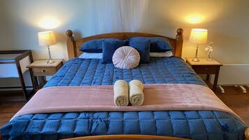 A neatly made bed with a blue quilt, two pillows, and a pink throw. There are two bedside lamps on wooden nightstands.