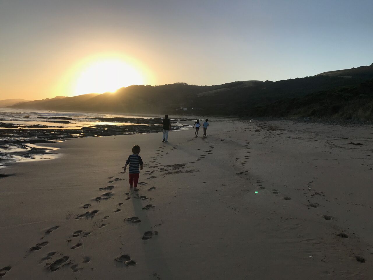 Uma praia com pegadas que se estendem em direção ao pôr do sol.
