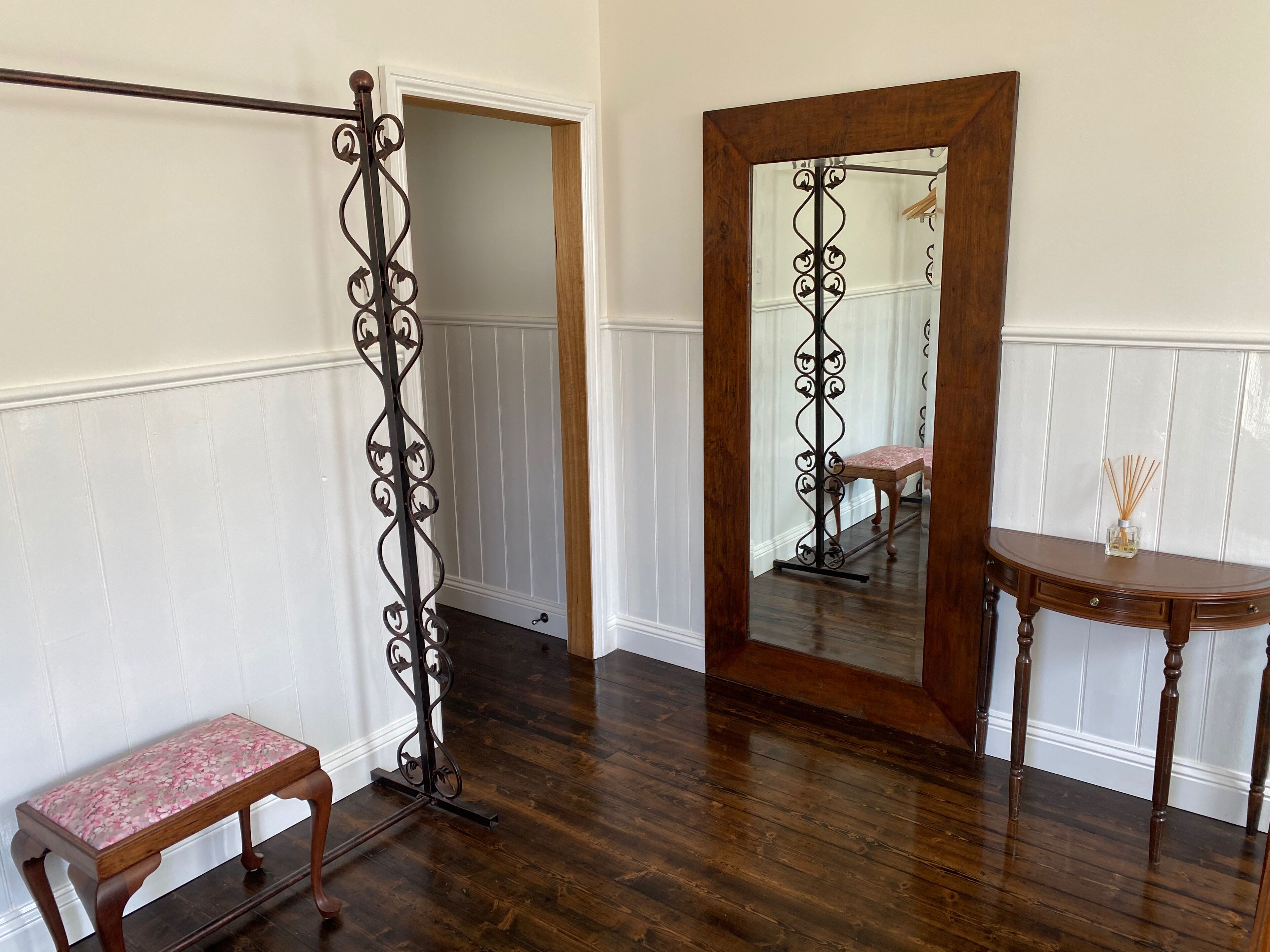 A room with a wooden bench, a mirror, and a decorative metal stand.