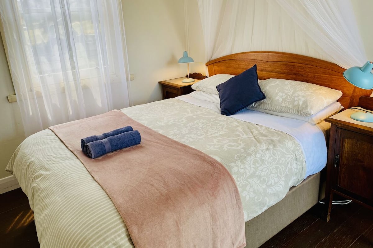 Una cama bien tendida con un edredón rosa, dos toallas azules y un cabecero de madera.