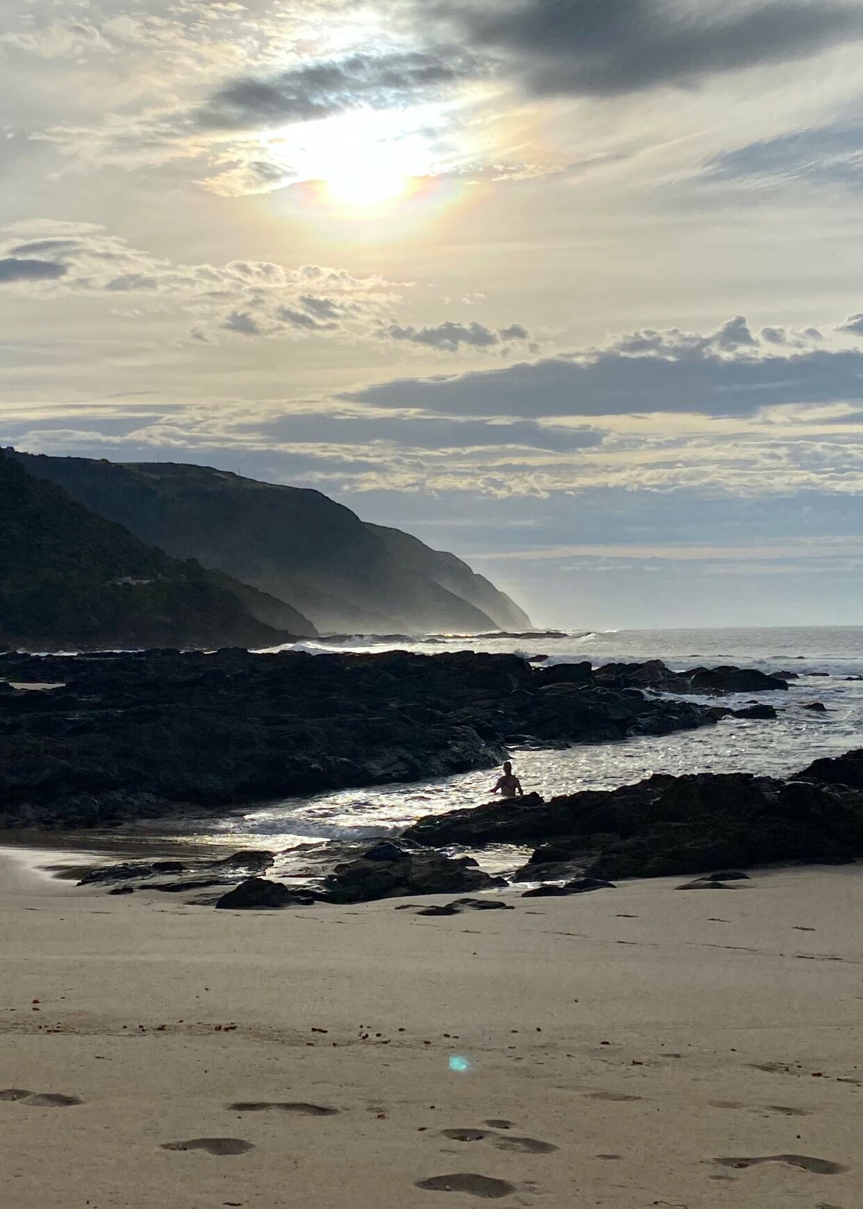 A beach with rocky terrain and a person sitting on the rocks.