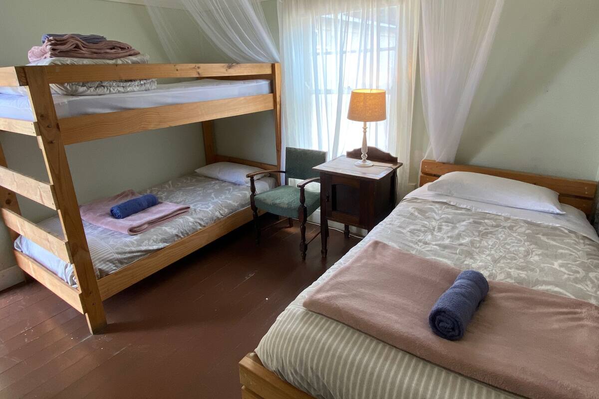 Una habitación con literas, una cama individual, un escritorio con lámpara y una silla.